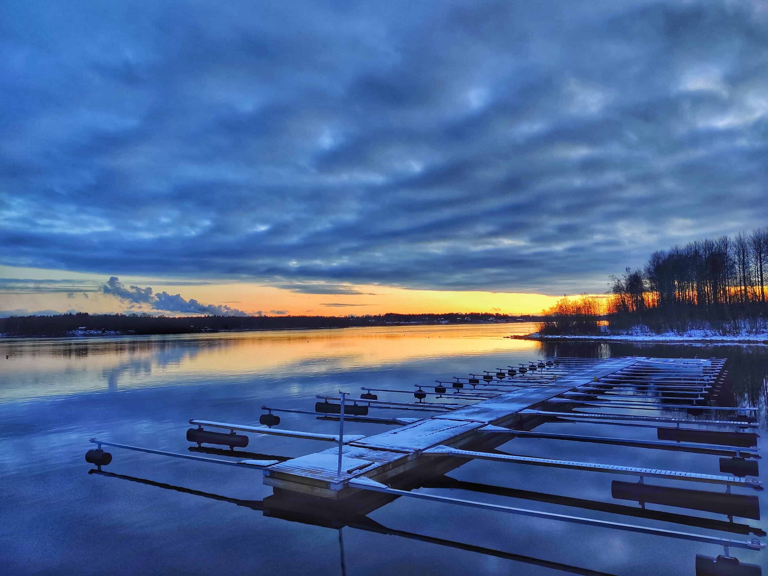 Tyhjä venesatama syksyn ensilumien aikaan, horisontissa auringonlasku.