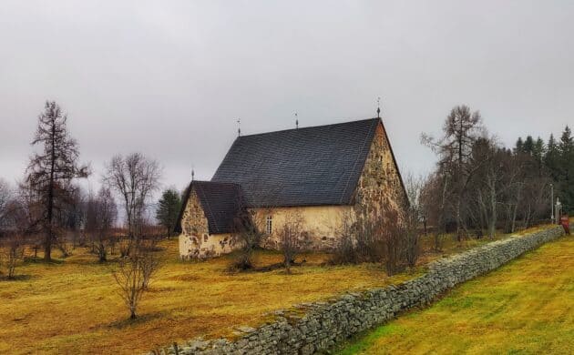 Keskiaikainen kivikirkko rinteessä, etualalla kiviaitaa.