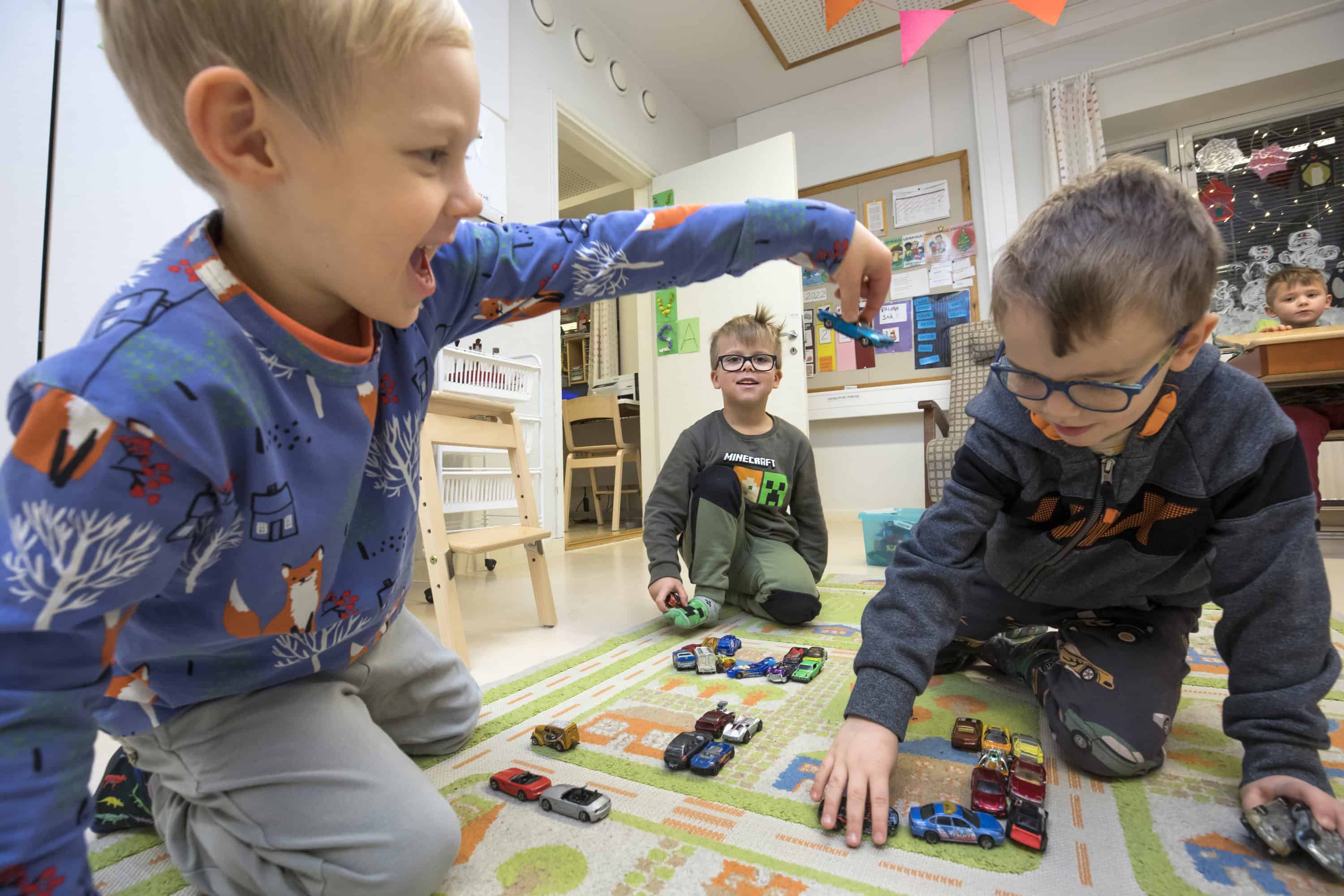 Kolme 5-6-vuotiasta poikaa leikkii autoilla lattialla.
