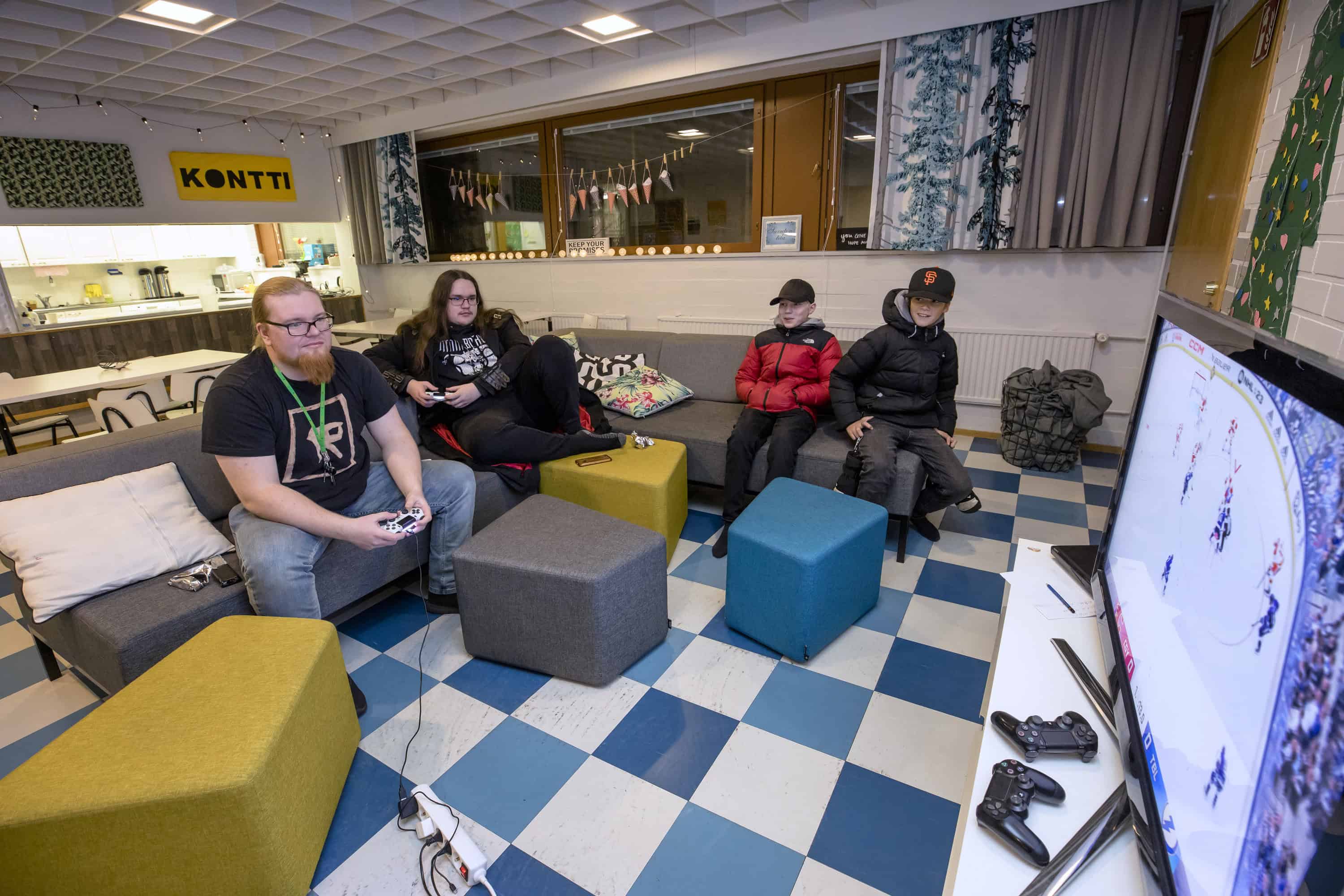 Kaksi nuorta miestä ja kaksi nuorta poikaa sohvilla katsomassa televisiota.