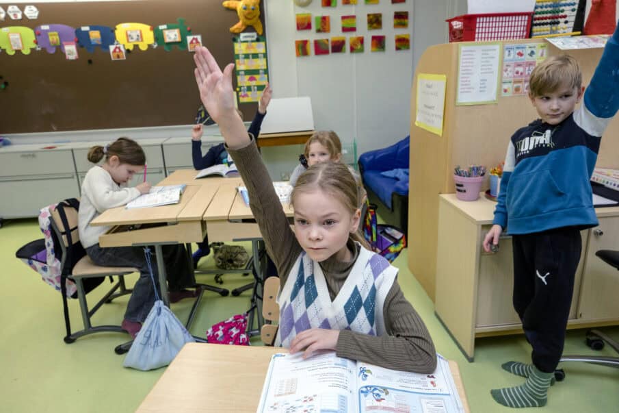 Tokaluokkalaisia luokassa. Etualalla istuva tyttö ja seisova poika, jotka viittaavat.