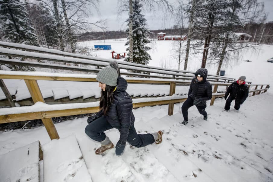 Kaksi nuorta naista ja yksi nuori mies nousemassa kuntoportaita. Talvinen kuva.