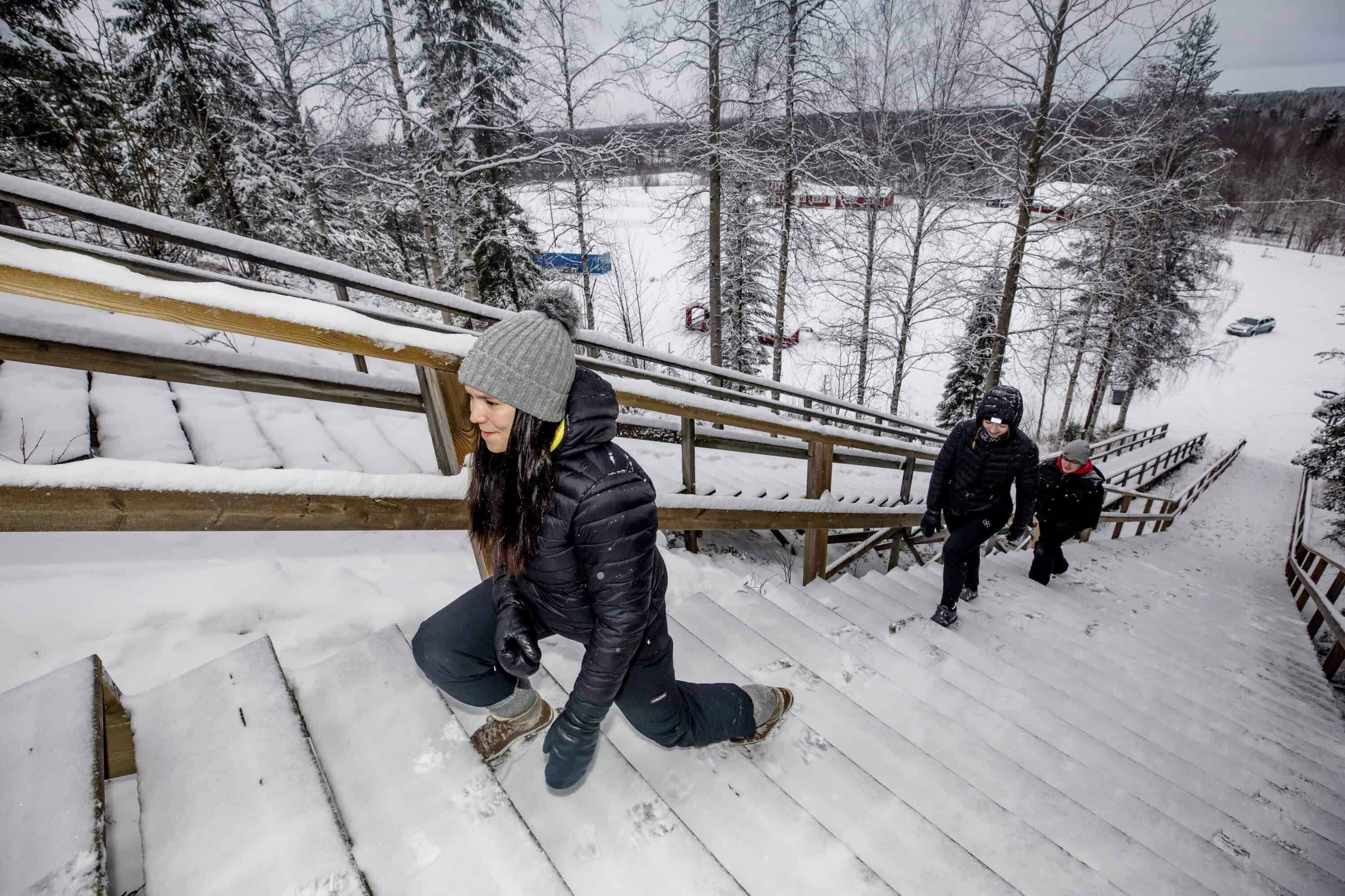 Kaksi nuorta naista ja yksi nuori mies nousemassa kuntoportaita. Talvinen kuva.