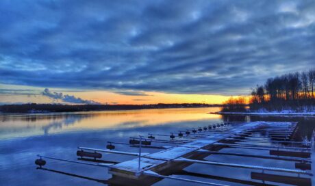 Tyhjä venesatama syksyn ensilumien aikaan, horisontissa auringonlasku.