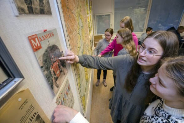Yläkoululaisia tutkimassa seinällä olevaa karttaa ja traktorinkuvaa. Viisi noin 15-vuotiasta tyttöä luokkahuoneessa.