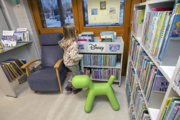 Pieni tyttö kirjaston lastenosastolla hyllyjen ääressä.