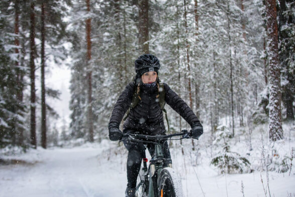 Nuori nainen ajaa maastopyörällä metsässä. Talvinen kuva.