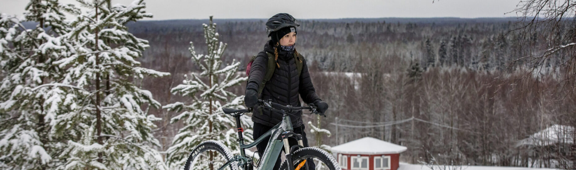 Nuori nainen seisoo maastopyörän vieressä mäellä. Talvinen kuva.