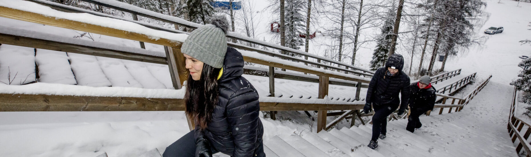 Kaksi nuorta naista ja yksi nuori mies nousemassa kuntoportaita. Talvinen kuva.